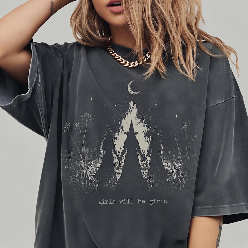 A woman wearing a black t-shirt with a graphic design featuring silhouettes of three figures against a night sky background.