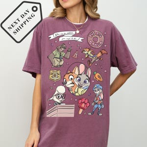 A person wearing a purple t-shirt with various cartoon characters and designs, including a character resembling a fox, a character resembling a rabbit, and a character resembling a police officer.