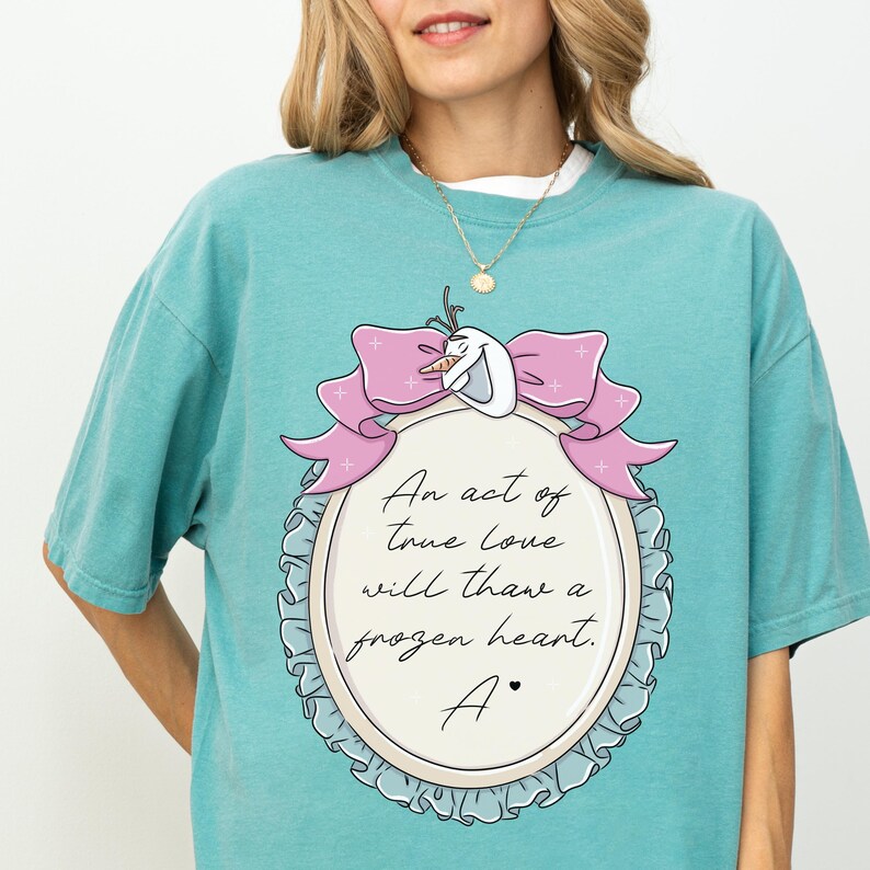 A woman wearing a teal t-shirt with a graphic design featuring a bow and a quote about love.