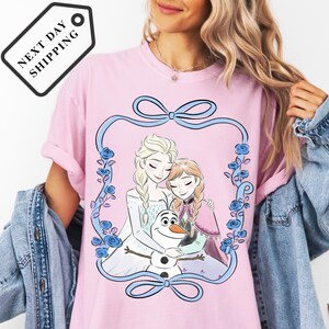 A woman wearing a pink t-shirt with a graphic of two women and a snowman.