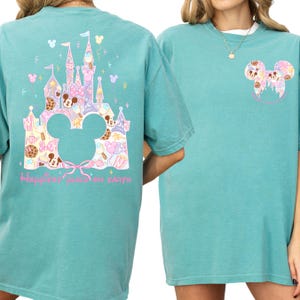 two turquoise t-shirts with Disney-themed designs. The t-shirt on the left has a castle and Mickey Mouse motif, while the t-shirt on the right has a Mickey Mouse motif. Both t-shirts have the text "Happiest place on earth" printed on them.