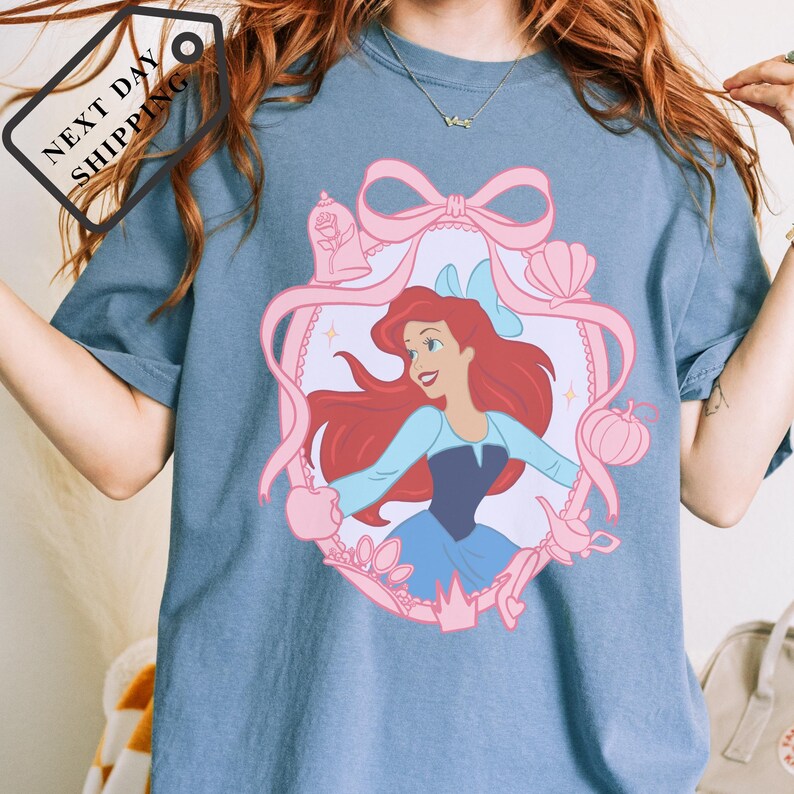 A person wearing a blue t-shirt with a pink bow and a cartoon image of a young girl with red hair.