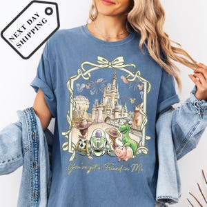 A woman wearing a blue t-shirt with a graphic design depicting a castle and various Disney characters, including a pig and a dinosaur.