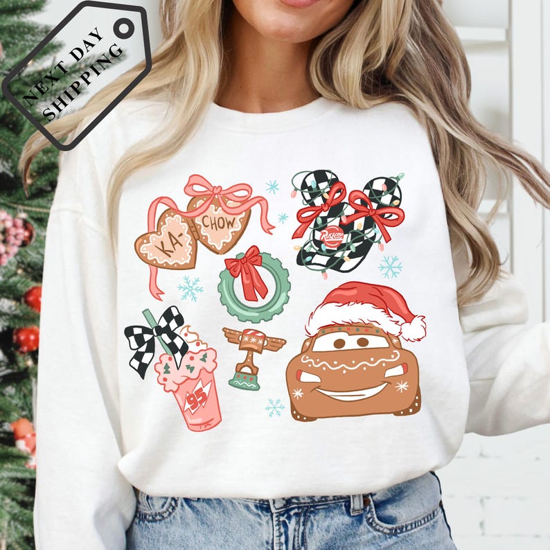 A woman wearing a white long-sleeved shirt with a Christmas-themed design featuring various holiday-related icons and characters, such as a Santa hat, a gingerbread man, and a car.