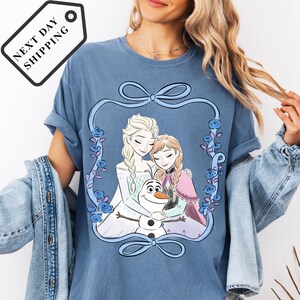 A woman wearing a blue t-shirt with a graphic design featuring two women and a snowman.