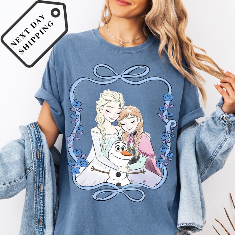 A woman wearing a blue t-shirt with a graphic design featuring two women and a snowman.