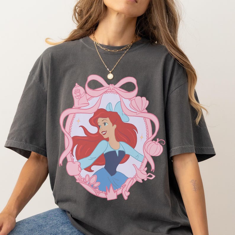 A woman wearing a gray t-shirt with a graphic of a cartoon character, specifically the Disney character Ariel from The Little Mermaid.