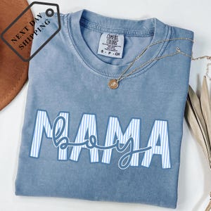 A blue t-shirt with the word "MAMA" printed on it, along with a necklace and a brown hat.