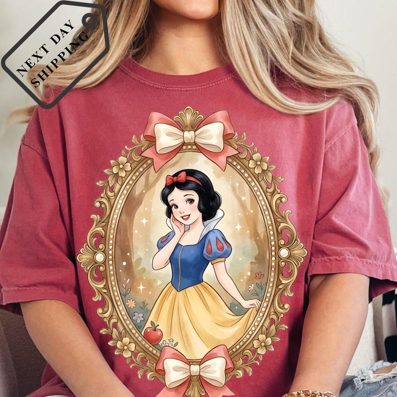 A woman wearing a red t-shirt with a framed illustration of Snow White, the Disney princess, on it.