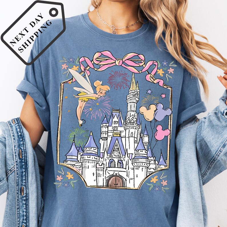 A woman wearing a blue t-shirt with a castle and fairy design printed on it.