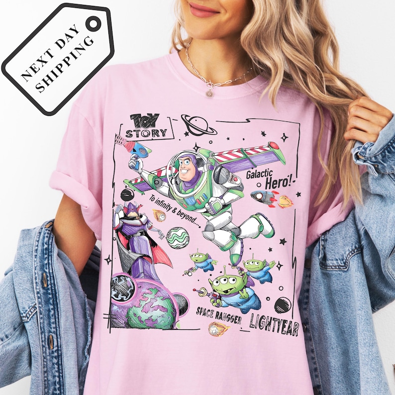 A woman wearing a pink t-shirt with a graphic design featuring characters from the Toy Story franchise, including Buzz Lightyear and a Galactic Hero, along with various space-themed elements.