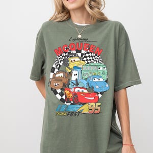 A person wearing a green t-shirt with a graphic design featuring various cartoon cars from the Cars movie franchise.