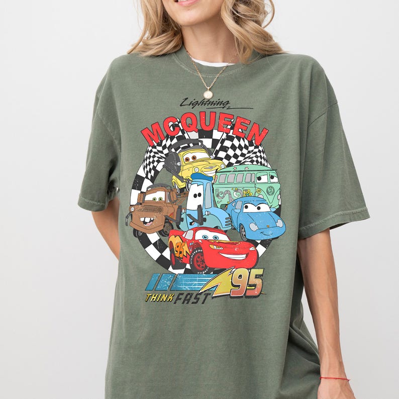 A person wearing a green t-shirt with a graphic design featuring various cartoon cars from the Cars movie franchise.