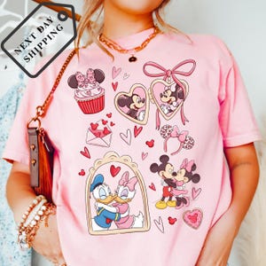A woman wearing a pink t-shirt with various Disney characters and heart-shaped designs printed on it.