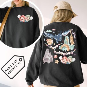 A person wearing a black sweatshirt with a colorful graphic design featuring Mario, a cat, and various other characters and elements.