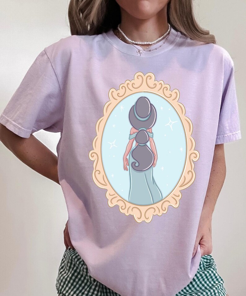 A woman wearing a purple t-shirt with a graphic of a woman in a mirror frame.