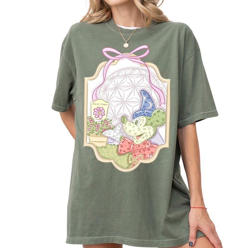 A woman wearing a green t-shirt with a colorful graphic design featuring a cartoon character and various decorative elements.