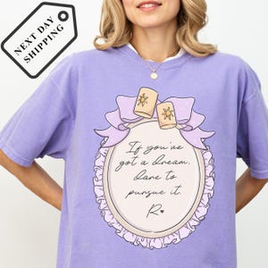 A woman wearing a purple t-shirt with a quote printed on it.
