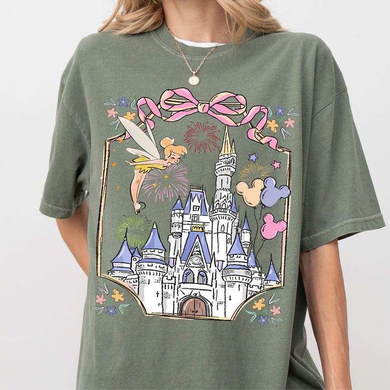 A green t-shirt with a graphic design depicting a castle surrounded by colorful flowers and a fairy.