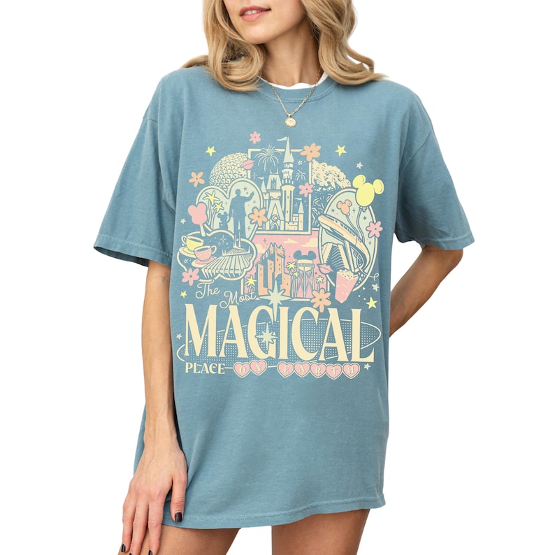 A woman wearing a blue t-shirt with a graphic design featuring various Disney-themed elements, including Mickey Mouse, a castle, and flowers.
