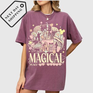 A woman wearing a purple t-shirt with a graphic design featuring various Disney-themed elements, including Mickey Mouse, the Eiffel Tower, and other iconic landmarks.