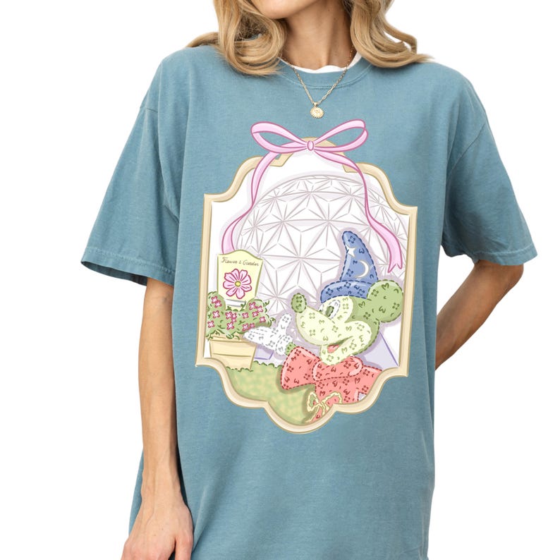A woman wearing a blue t-shirt with a colorful graphic design featuring a flower, a bow, and various other decorative elements.