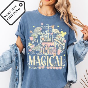 A woman wearing a blue t-shirt with a graphic design featuring various Disney-themed elements, such as Mickey Mouse, Minnie Mouse, and a castle.