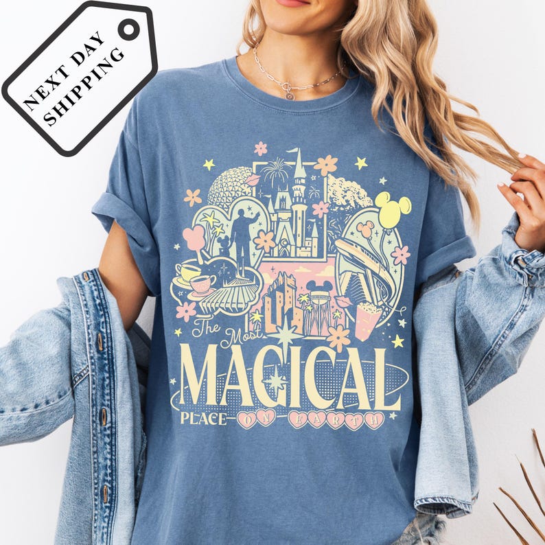 A woman wearing a blue t-shirt with a graphic design featuring various Disney-themed elements, such as Mickey Mouse, Minnie Mouse, and a castle.