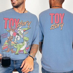 A man wearing a blue t-shirt with a colorful graphic of Woody and Buzz Lightyear from the Toy Story movie.