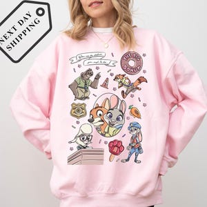 A woman wearing a pink sweatshirt with a cartoon character design featuring various cartoon animals and objects.