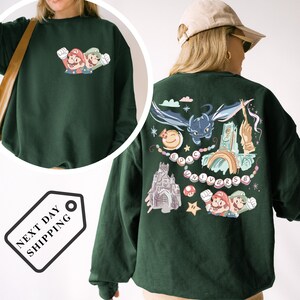 A green sweatshirt with a colorful graphic design featuring Mario and other characters, along with various other elements such as a castle, a dragon, and a rainbow.