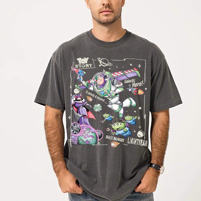 A man wearing a gray t-shirt with a colorful graphic design featuring characters from the Toy Story franchise, including Buzz Lightyear and other beloved characters.