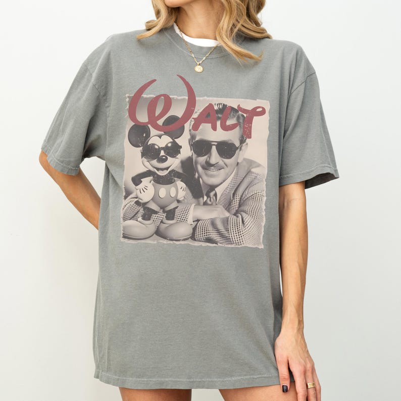 A person wearing a gray t-shirt with a graphic design featuring a man and a child, along with the text "Walt Disney".