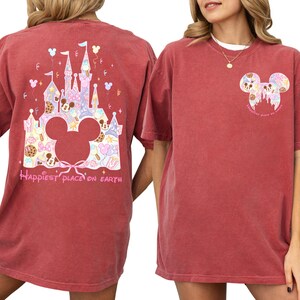 two women wearing red t-shirts with Disney-themed designs. The t-shirts have a castle and Mickey Mouse motif, and the text "Happiest place on Earth" is printed on the back.