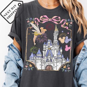 A person wearing a gray t-shirt with a graphic design depicting a castle and fireworks.