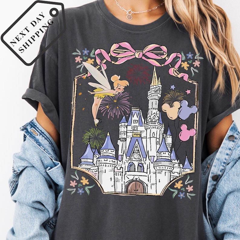 A person wearing a gray t-shirt with a graphic design depicting a castle and fireworks.