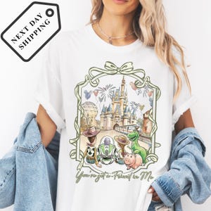 A woman wearing a white t-shirt with a graphic design featuring a castle, a dinosaur, and various other characters.