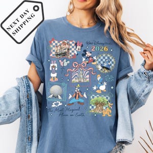 A woman wearing a blue t-shirt with various Disney characters and landmarks printed on it, including Mickey Mouse, Minnie Mouse, Donald Duck, and Eiffel Tower.