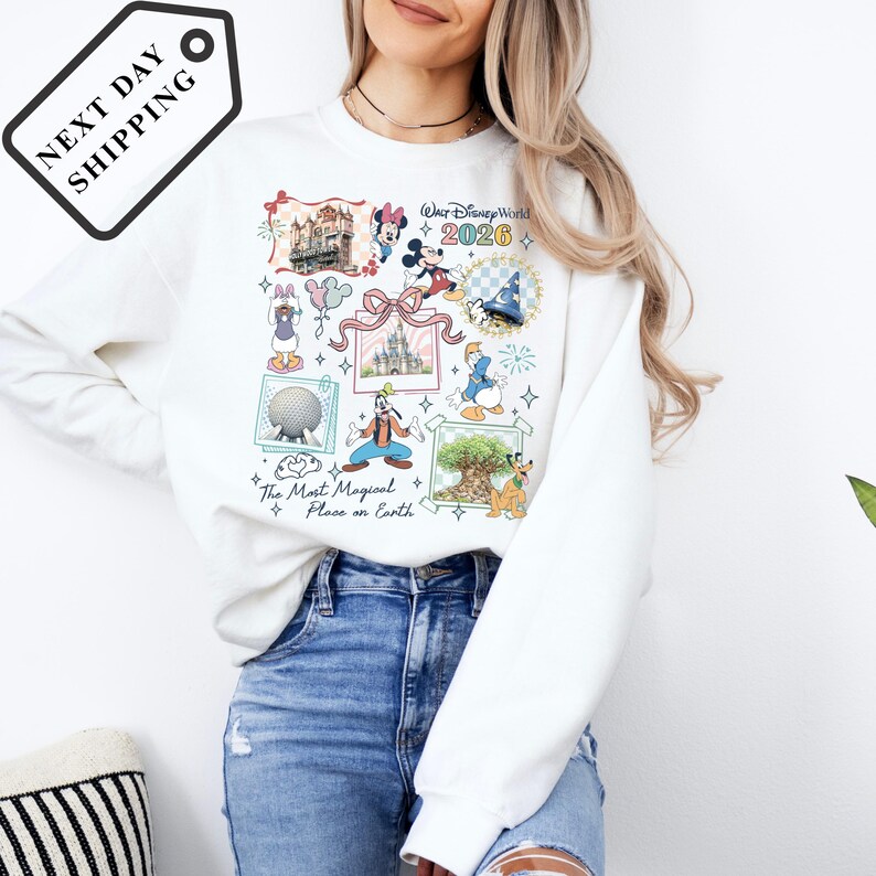 A woman wearing a white sweater with a colorful graphic design featuring Disney characters and landmarks, such as Eiffel Tower, Mickey Mouse, and the Disney World logo.