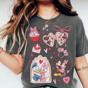 A woman wearing a gray t-shirt with various Disney characters and heart-shaped designs printed on it.