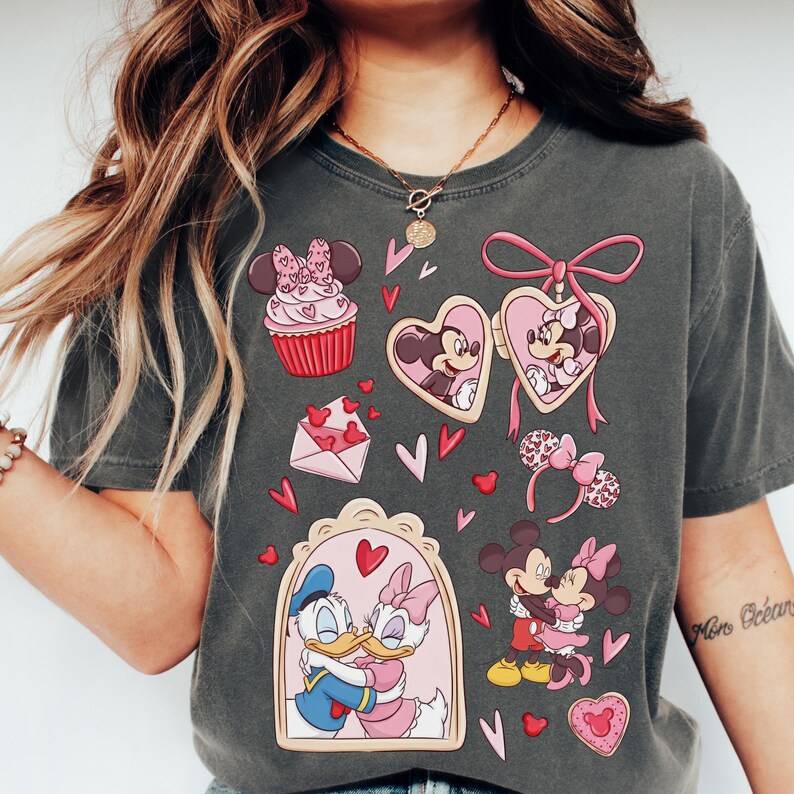 A woman wearing a gray t-shirt with various Disney characters and heart-shaped designs printed on it.