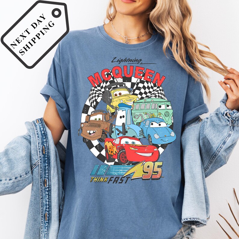 A person wearing a blue t-shirt with a graphic of various cartoon cars from the Cars movie franchise, including Lightning McQueen and other characters.