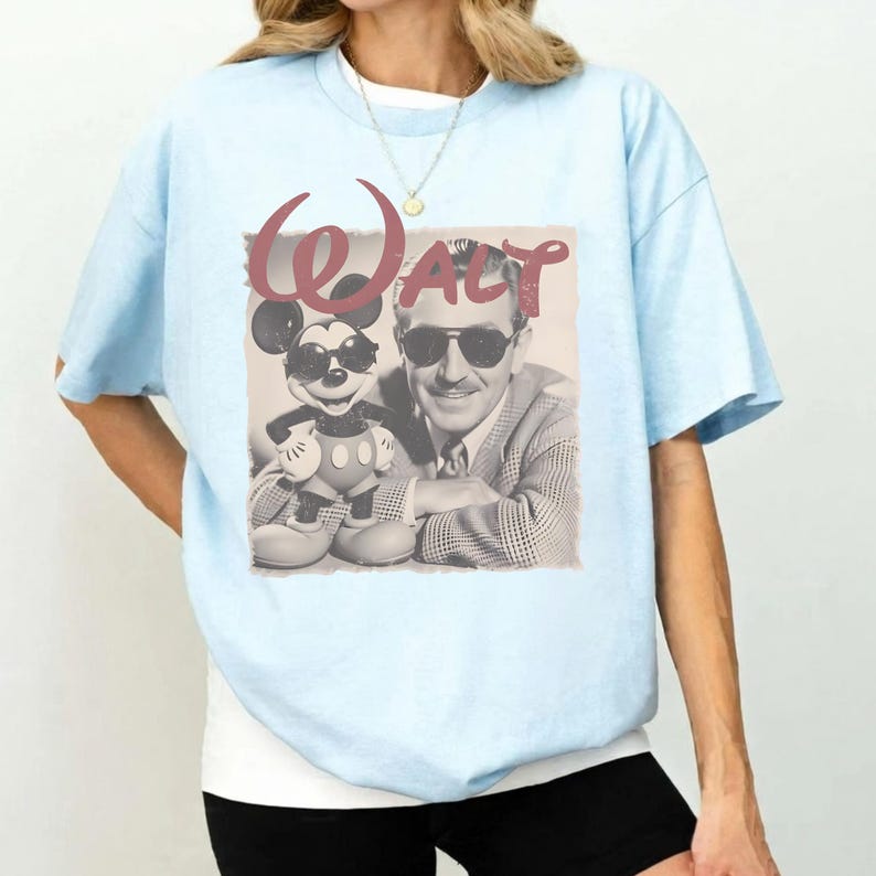 A woman wearing a light blue t-shirt with a graphic design featuring a man and a character from Disney.