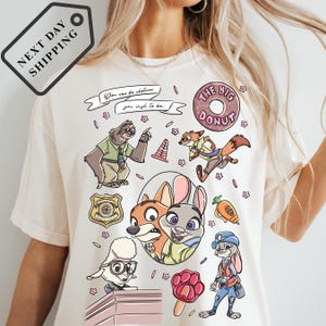 A white t-shirt with a colorful graphic design featuring various cartoon characters, including a police officer, a fox, and other animals.