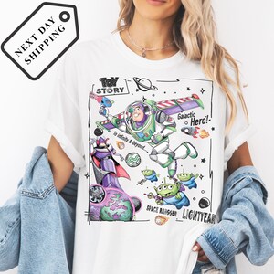 A person wearing a white t-shirt with a colorful graphic design featuring characters from the Toy Story franchise, including Buzz Lightyear and a group of smaller alien characters.