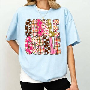 A woman wearing a light blue t-shirt with the text "GOBBLE GOBBLE" printed on it.