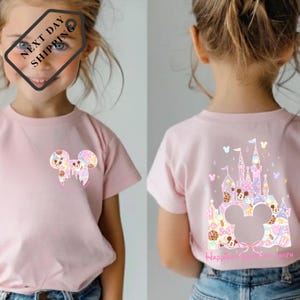 A young girl wearing a pink t-shirt with a Mickey Mouse design and a castle graphic on the back.