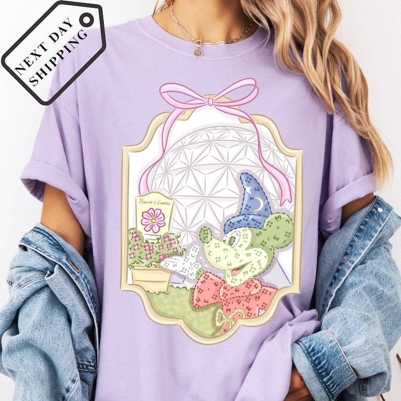 A person wearing a purple t-shirt with a graphic design featuring a cactus, flowers, and a castle-like structure.