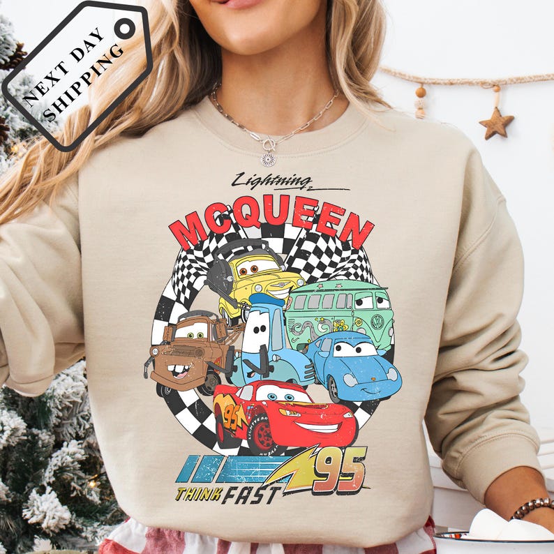A woman wearing a sweatshirt with a graphic of the Disney Pixar Cars characters Lightning McQueen and other cars from the movie "Cars".