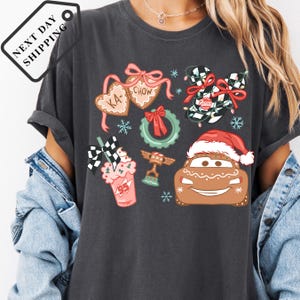 A person wearing a gray t-shirt with various Christmas-themed graphics and icons, including a Santa hat, gingerbread houses, and other festive elements.